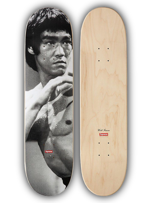 A skateboard deck shown from both sides: one side features a black-and-white graphic print of Bruce Lee, and the other side shows a natural light wood grain finish with grip dots and a small red Supreme logo near the tail.